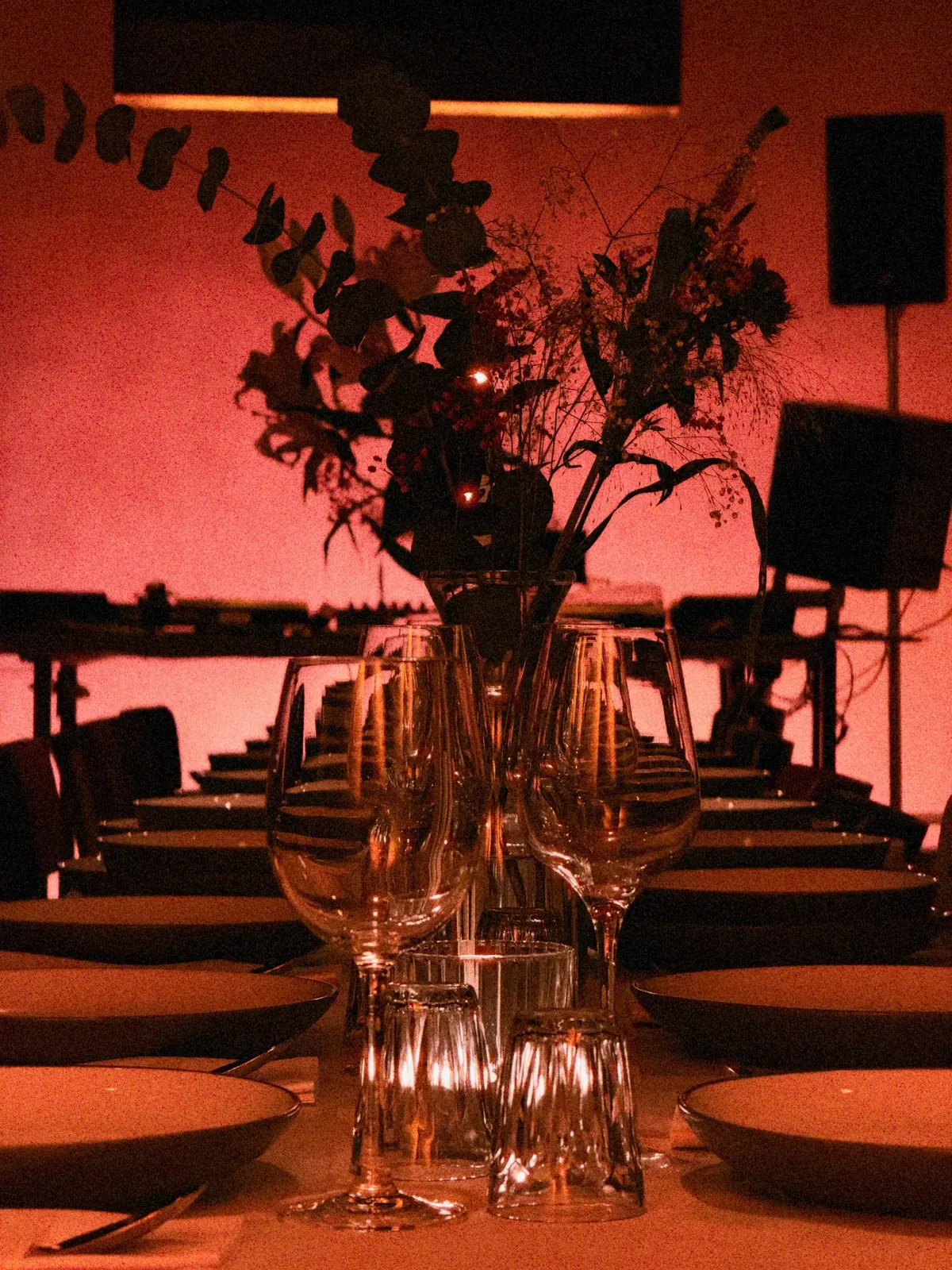 Gläser, Teller und Blumen auf dem Dinnertisch bei warmem Licht